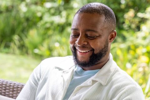 African american man smiling and relaxing on rattan patio chair among lush garden greenery