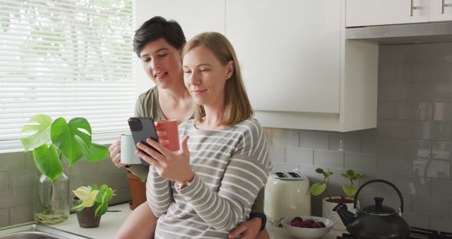 Mid-adult couple enjoying morning coffee together in sunny modern kitchen. Man and woman reading tablet and smiling. Suitable for depictions of home lifestyle, technology use, and relationship moments.
