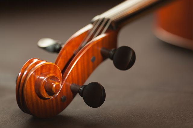 Detailed image of a violin's scroll and tuning pegs showcasing the craftsmanship of the musical instrument. Ideal for use in articles, advertisements, or educational materials about classical music, art, or instrument craftsmanship. Perfect for promoting musical lessons, instrument sales, or concerts.