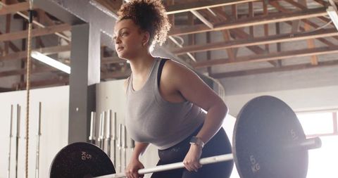 Determined woman lifting barbell in sunlit industrial gym performing deadlift for strength