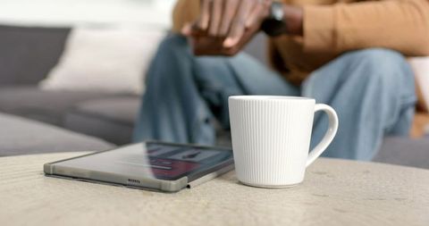 African American man adjusting watch beside white mug and tablet on coffee table