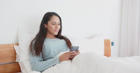 Relaxing Woman Using Smartphone in Bright Bedroom Setting