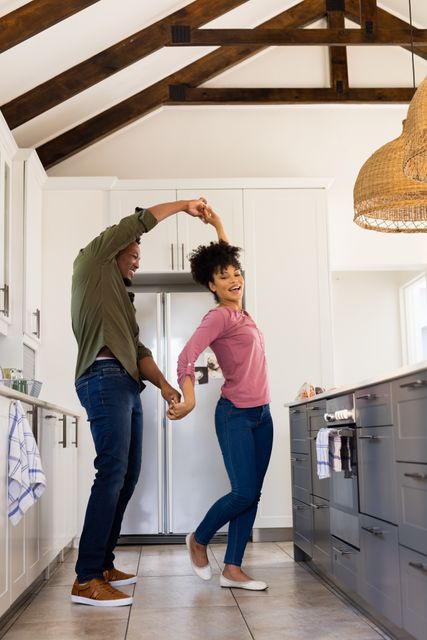 This image depicts a joyful biracial couple dancing together in a modern kitchen. The scene captures a moment of fun and togetherness, making it perfect for use in lifestyle blogs, advertisements promoting home products, or articles about relationships and family life. The bright and airy kitchen setting adds a contemporary feel, suitable for content related to home decor or cooking.