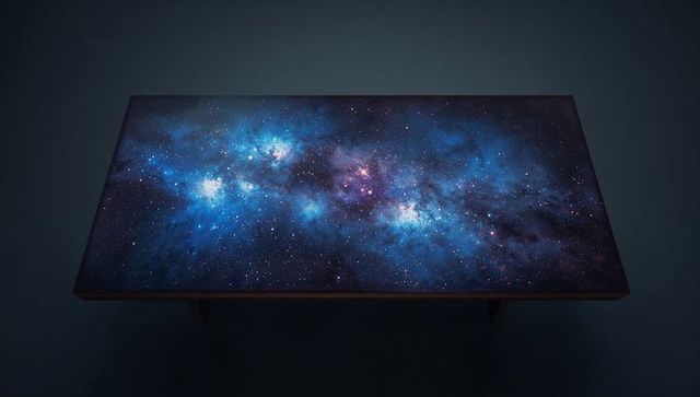 Wooden table displaying glowing galaxy surface art with starfield nebula and reflections