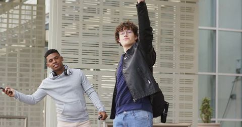Diverse young travelers in transit plaza pulling rolling luggage and checking smartphones