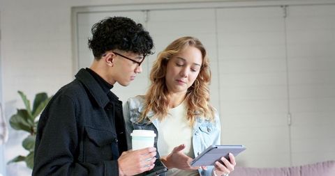 Young coworkers collaborating over tablet and coffee in bright modern office lounge