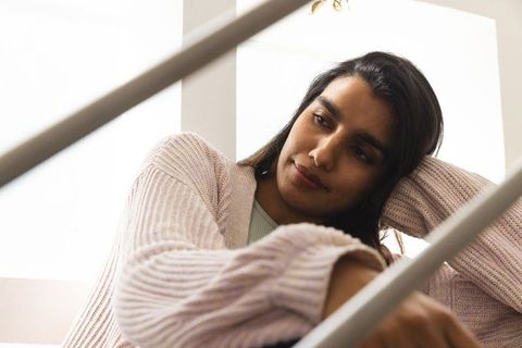 Contemplative female leaning on stair railing by window indoors
