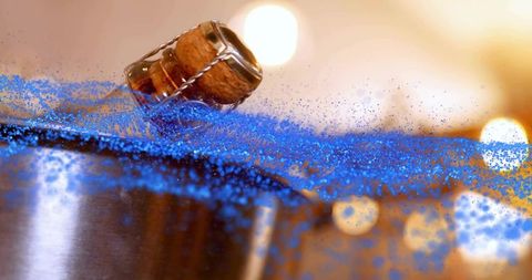 Blue glitter scattering from champagne cork on reflective metal rim, macro party detail