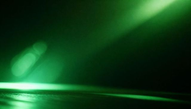 Emerald laser beam cutting diagonal shaft with thin floor reflection and soft bokeh glow