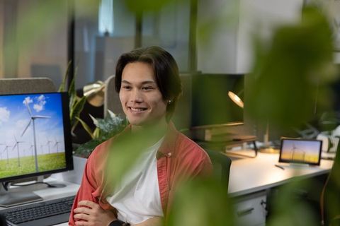 Young asian professional smiling in modern green office with wind energy monitors