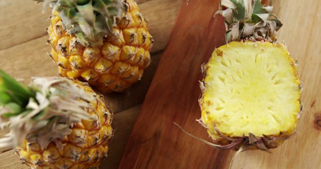 A ripe pineapple is sliced on a wooden cutting board, showcasing its juicy yellow interior, with copy space. Fresh pineapples like this are often used in culinary dishes for their sweet and tangy flavor.