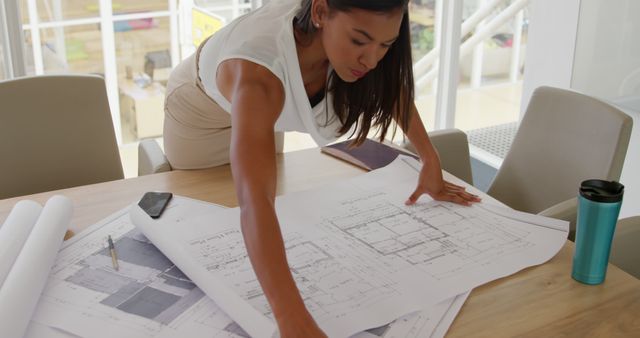 An architect reviews blueprints at her office desk. Precision and attention to detail are crucial in her role as she plans a new structure.