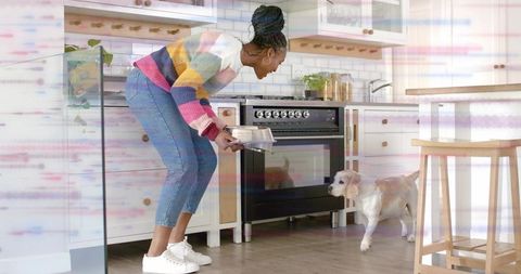 Woman feeding small dog in bright kitchen holding bowl, cozy home lifestyle moment
