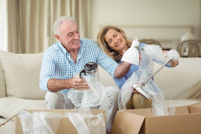 Smiling senior couple unpacking carton boxes in living room at new home
