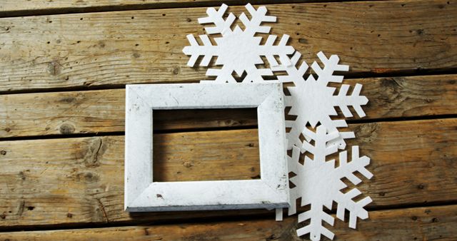 Rustic wooden background with three white snowflakes and an empty picture frame. Perfect for holiday greetings, winter decorations, or Christmas-themed designs. Suitable for DIY craft ideas, festive blogs, and seasonal marketing materials.