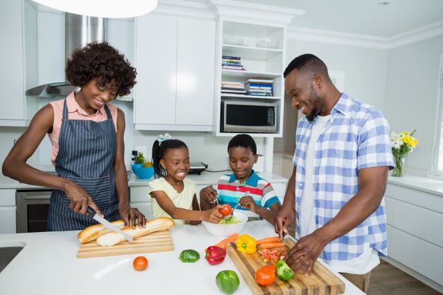 This image shows a happy family of four preparing a meal together in a modern kitchen. The parents and children are chopping vegetables and smiling, indicating a joyful and collaborative atmosphere. This image can be used for promoting family bonding, healthy eating, cooking classes, kitchen appliances, and lifestyle blogs.