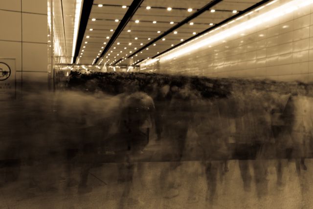 Blurred crowd of people moving through a hallway, creating a sense of motion and urgency. Sepia tone gives a vintage feel. Useful for depicting urban life, city hustle, commuting scenarios, or concepts of speed and movement in modern living.