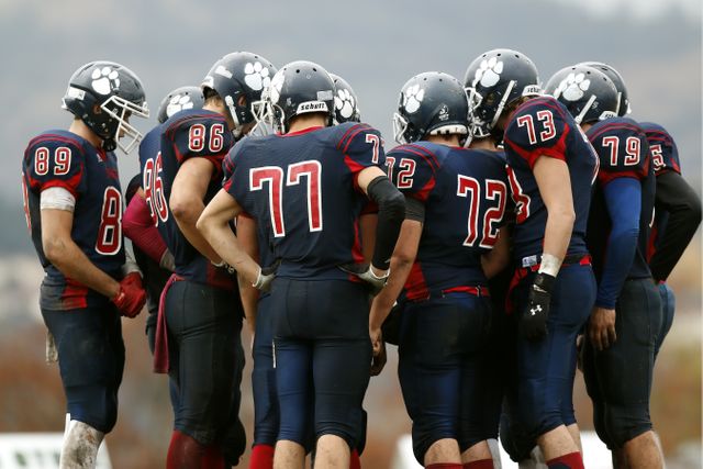 Team huddling on field during a football game. Great for illustrating teamwork, sports strategies, or athletic dedication. Suitable for advertisements, athletic program covers, and articles about sportsmanship.