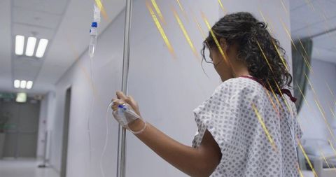 Child patient walking with iv pole in hospital corridor wearing patient gown and iv line