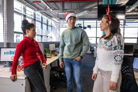 Coworkers chatting and celebrating in modern open office wearing Santa hat and festive sweaters
