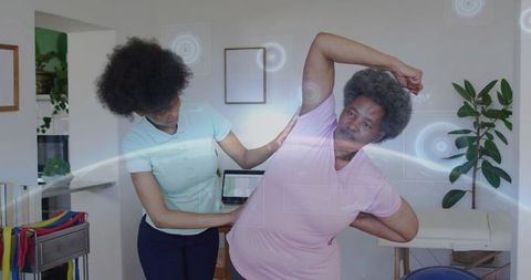 Female therapist supporting older woman doing assisted side stretch for mobility training