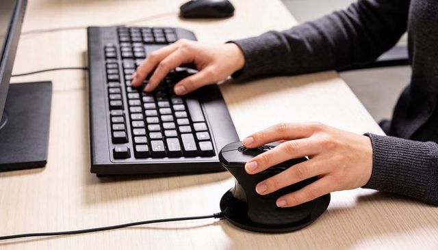 Right hand using vertical ergonomic mouse with keyboard on modern office desk close-up