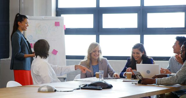 Image depicts a diverse team in a modern office environment engaging in an energetic meeting. The team members are collaborating, discussing ideas, and using technology and a whiteboard for a presentation. This image is great for portraying teamwork, business meetings, and professional collaboration in promotional materials, corporate websites, and business presentations.