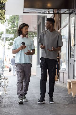 Young african american men walking talking on urban sidewalk holding coffee with headphones