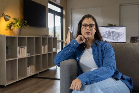 Woman sitting on sofa in home office viewing architectural floor plan on monitor