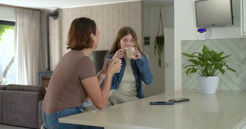 Friends chatting and sipping coffee at kitchen island in sunlit open-plan home interior