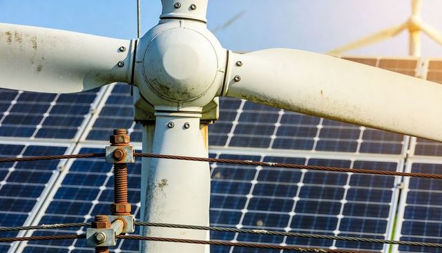 Weathered wind turbine hub showing blade, bolts and cables over solar panel array, hybrid energy