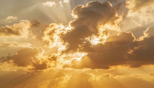 Golden sunbeams streaming through backlit cumulus clouds at dramatic sunset
