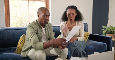 Diverse Couple Analyzing Financial Document on Couch