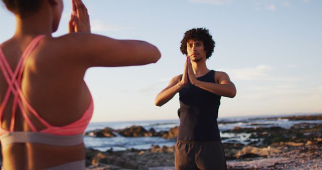 African american couple practicing yoga together on the rocks near the sea. love and relationship concept