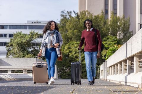 Young students walking on campus bridge pulling rolling luggage and backpacks