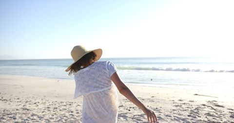 Woman in straw hat enjoying sunny beach with arms outstretched