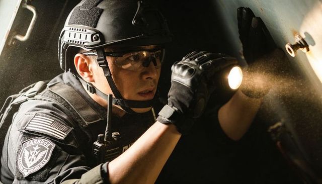 Tactical officer inspecting confined metal compartment with flashlight, low-light security