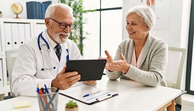Senior patient consulting friendly doctor reviewing tablet together in bright clinic