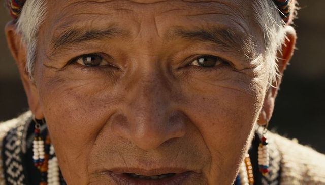 Closeup senior hispanic man wearing woven hat and beaded earrings, sunlit wrinkles
