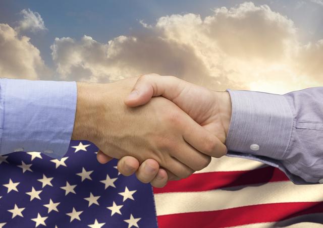 Business executives shaking hands against the backdrop of an American flag symbolize agreement, trust, and partnerships. This image is suitable for illustrating themes of business deals, professional collaborations, American business culture, and patriotic business practices. It can be used on websites, presentations, articles, and advertisements relating to business, finance, patriotism, and corporate success.