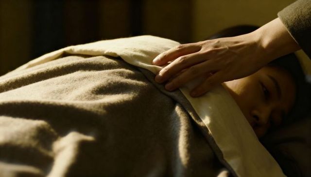 Comforting hand smoothing wool blanket over resting asian woman in warm intimate closeup