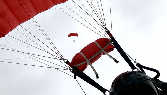 Close-up parachute rig with red reserve pack and helmet, dramatic low-angle sky view