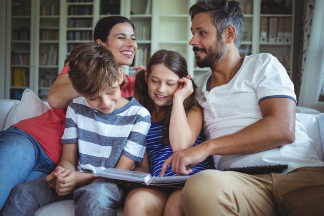 Family sitting on sofa, enjoying time together while looking at a photo album. Ideal for themes related to family bonding, home life, and creating memories. Suitable for use in advertisements, family-oriented content, and lifestyle blogs.