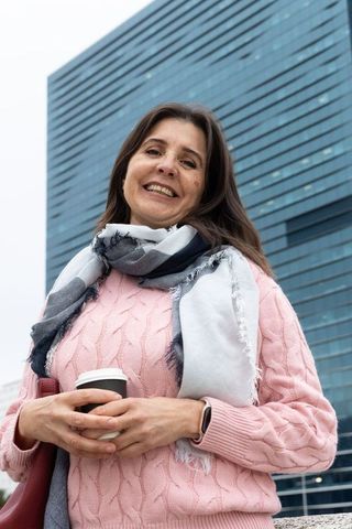Smiling middle-aged woman standing in office plaza holding coffee wearing pink sweater
