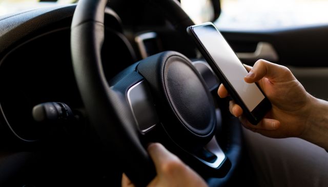 Man holding smartphone while test driving car, focusing on technology and driving. Useful for topics related to driving safety, technology use in vehicles, distracted driving, automotive industry, and modern transportation.