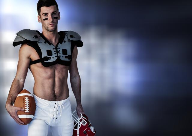 This image features a male athlete standing confidently while holding a rugby ball and helmet. He is wearing protective gear, showcasing his muscular physique and determination. The blurred background emphasizes the subject, making it ideal for use in sports-related advertisements, fitness promotions, and motivational posters.