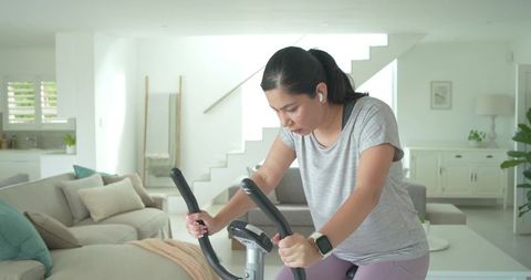 Young woman doing indoor cycling workout on stationary bike in modern sunlit living room