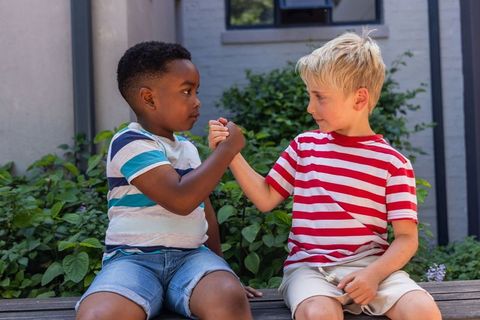 Two boys clasping hands on wooden bench in front yard sharing friendship and respect