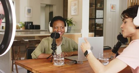 Diverse co-hosts recording podcast in modern kitchen with condenser mics and laptop