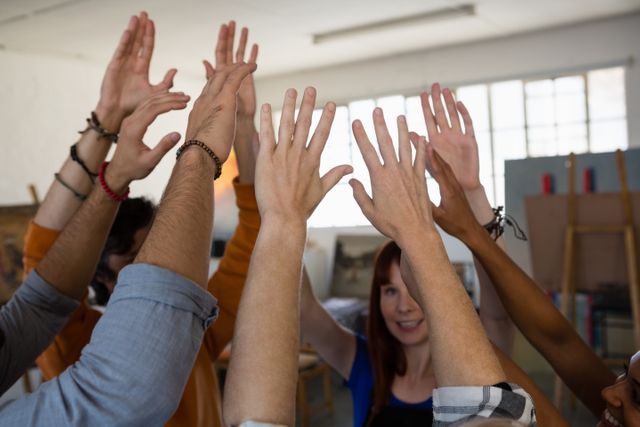 Group of friends raising their hands in celebration in an art class. Ideal for themes related to teamwork, creativity, and positive group dynamics. Perfect for educational materials, team-building promotions, and creative workshop advertisements.